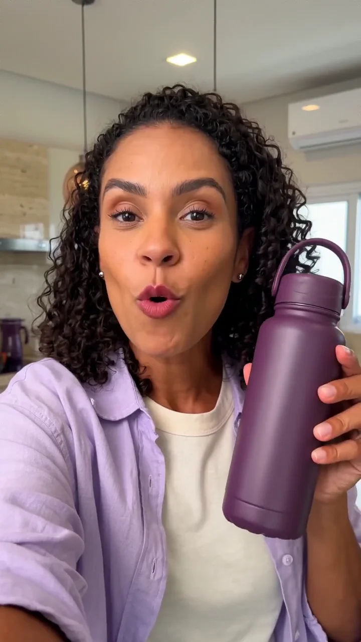 Uma criadora apresenta uma garrafa térmica violeta, demonstra o acabamento e a alça e faz uma chamada para compra em português.